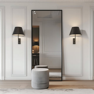 Facet straight-edged full-length mirror with sleek black frame in a minimalist room, reflecting elegant wall paneling and soft lighting from a wall-mounted lamp.
