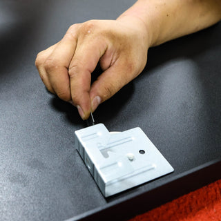 Close-up of a worker securing a metal hook onto the back of a full-length mirror, preparing it for wall mounting at the C&F Creations factory.
