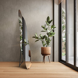 Cascade Irregular Frameless Full-Length Freestanding Mirror (160x60cm), displayed in a modern room with wooden flooring, positioned beside a potted plant and large windows.