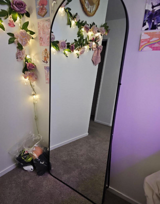 Ana’s five-star review of the Svelte Arched Full-Length Mirror from C&F Creation. She describes it as the best mirror she’s purchased in a long time and highly recommends it. The mirror is styled in a cozy room with decorative lighting and floral accents.