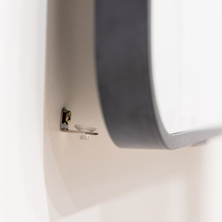 Close-up showing the final installation step of a full-length mirror. The top hooks are secured, and the bottom of the mirror is gently lifted and placed onto the heavy-load support screw to ensure safe and stable wall mounting.