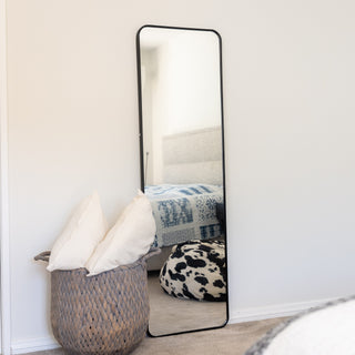 Lithe X Full-Length Mirror (155x45cm) with a sleek black frame, elegantly positioned in a modern bedroom. This versatile mirror can be used as a wall-mounted, freestanding, or floor mirror, adding a minimalist touch to any space. Styled with cozy décor, including a woven basket and plush pillows. | C&F Creation
