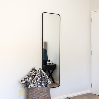 A modern Lithe X Full-Length Mirror (155x45cm) elegantly mounted on a bedroom wall. This wall mirror features a slim black frame, providing a stylish and space-saving solution for small bedrooms, dressing rooms, or hallways. Its freestanding and wall-mounted versatility makes it a perfect home décor addition. The high-quality glass delivers a crystal-clear reflection, enhancing any interior setting. | C&F Creation