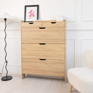 Front view of the Risa Slim Shoe Cabinet in oak finish, styled in a modern living space with a black floor lamp, framed artwork, and a cream accent chair. The slim, tall design with two top drawers and three spacious compartments makes it a stylish and practical storage solution for entryways or bedrooms.