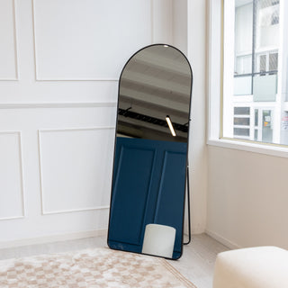 The Svelte X arched full-length mirror leaning against a white wall, reflecting elegant decor and soft natural lighting in a cosy space.