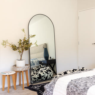 The Titan arched full-length mirror (180x80 cm) with a sleek black frame, leaning elegantly against a neutral-toned bedroom wall. A perfect statement piece for enhancing space and style in any modern home. | C&F Creation