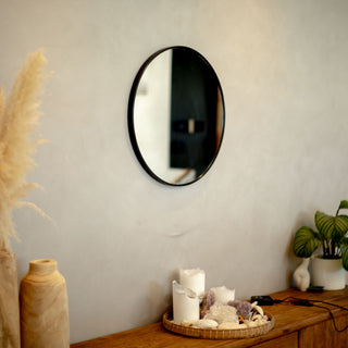 Valor Round Wall Mirror with a sleek black aluminium alloy frame, mounted above a wooden console table decorated with candles, pampas grass, and greenery | C&F Creation