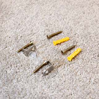 A complete wall mounting kit for full-length mirrors, including screws, yellow wall plugs, metal brackets, and rubber buffers laid out on a beige carpet — ideal for secure mirror installation.