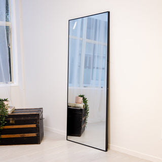 Front-facing image of the Zenith X full-length mirror 180x80cm, with a bold black frame and crisp reflection, styled with green foliage and neutral tones.