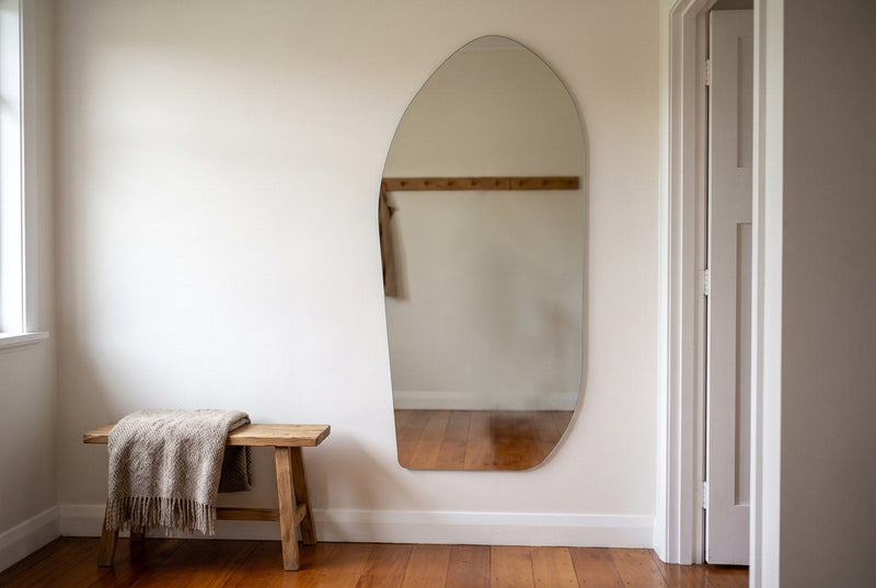 Cascade X irregular frameless 200 x 100cm mirror hung upright on a warm white hallway wall in a New Zealand bungalow, its straight right edge parallel to a white door frame, rimu floorboards and an oak bench to the left