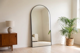 Grandeur X black arched full length mirror, 200 x 100cm, leaning at a gentle angle against a white plasterboard wall in a New Zealand living room, its base set out from the skirting board on an oak floor