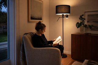 Floor reading lamp NZ, Lumen Duo floor lamp with its focused reading arm lighting an open book on a linen armchair in a New Zealand living room at dusk