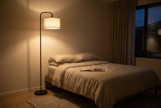 Bedroom floor lamps NZ — Marceau linen drum floor lamp glowing warm beside a made bed in a New Zealand bedroom at night, ceiling light off