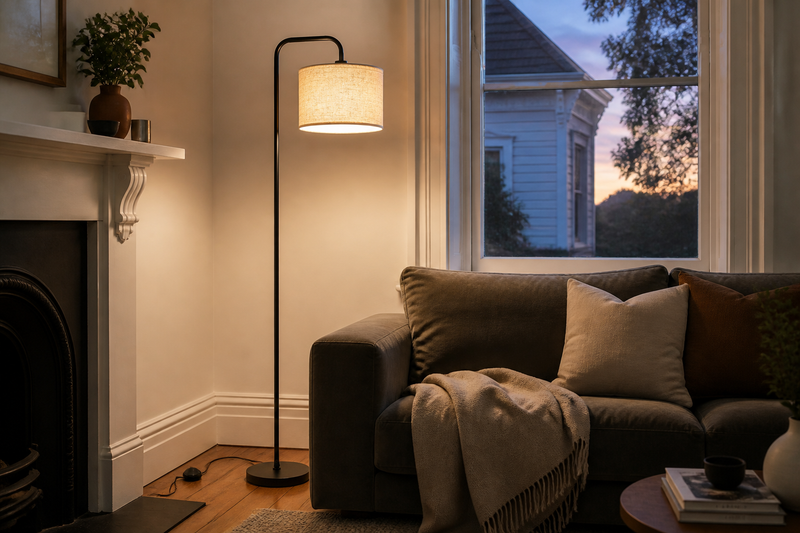 Floor lamps Auckland, Marceau Linen Drum floor lamp with black curved arm and oatmeal linen drum shade glowing beside a sofa in a renovated Auckland villa living room at dusk
