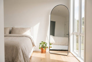 Mirror shop NZ, Titan arched full length mirror with black frame leaning against the wall of a bright New Zealand bedroom, the kind of mirror people search mirror shop near me hoping to find