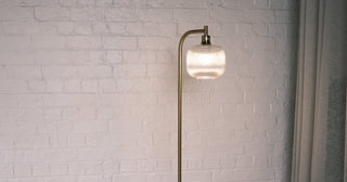 Solara Fluted Lantern Floor Lamp glowing warmly in a modern NZ living room with white brick wall and cream sofa | C&F Creation