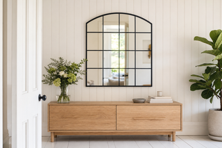 Le Vue arched window pane wall mirror hung above an oak sideboard in a white panelled room