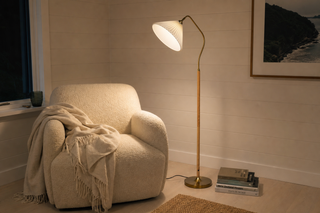 Floor standing lamp in a New Zealand reading nook: the Aurelia pleated fabric lamp leaning its cream shade out over a boucle armchair
