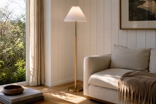 Standing lamp NZ — the Luma straight-pole standing lamp with a pleated white shade beside a linen sofa in a New Zealand weatherboard lounge