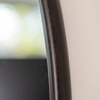 Close-up view of the Aure round wall mirror in black, showcasing the fine texture and 22 mm depth of its durable PS frame. The soft natural lighting highlights the smooth curvature and refined craftsmanship of the frame edge.