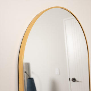 Close-up of the Aurelia arched full-length mirror, showing the smooth gold aluminium frame and elegant curved top edge.