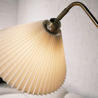 Detailed close up of the Aurelia floor lamp’s pleated fabric shade, showing the soft warm glow and brushed brass connector against a light textured wall.
