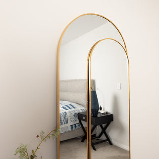 Close-up angled view of the Aurelia arched full-length mirror set with slim gold frames, reflecting a modern bedroom scene.