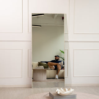 The Branewood 180x80cm full-length mirror with a wood-textured PS frame and 4mm clear glass, shown placed against a white panelled wall reflecting a stylish living area. This versatile mirror can be securely wall-mounted or used as a floor mirror, offering a natural, modern touch to New Zealand interiors.