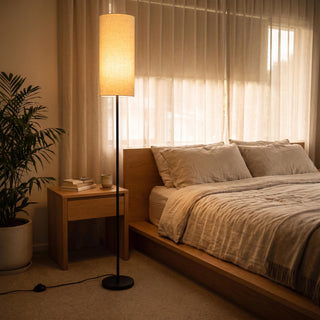 Chandelle Linen Column Floor Lamp casting a soft warm glow beside the bed in a cosy New Zealand bedroom