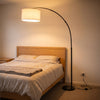 Flore Black Arc Floor Lamp arching over the foot of the bed in a cosy bedroom