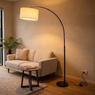 Flore Black Arc Floor Lamp glowing warm beside a sofa in a New Zealand living room