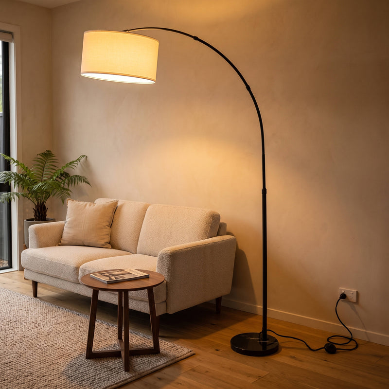Flore Black Arc Floor Lamp glowing warm beside a sofa in a New Zealand living room