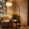 Flore Black Arc Floor Lamp curving over an armchair to light a relaxed reading corner