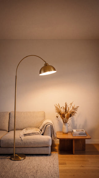 New floor lamp range mobile hero, Orsay gold arc floor lamp glowing warm beside a sofa in a New Zealand living room