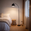 Saturne Black Globe Arc Floor Lamp casting a soft glow beside a bed in a calm bedroom