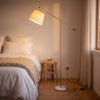 Vienna Brass Marble Base Floor Lamp casting a soft glow beside a bed in a calm bedroom