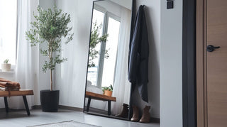 Full-length mirror with sleek black frame reflecting natural light in a modern living room, enhancing the decor with its minimalist design.