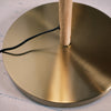 Close up of the Luma Pleated Floor Lamp’s brushed brass base with a natural wood pole and black cord detail.