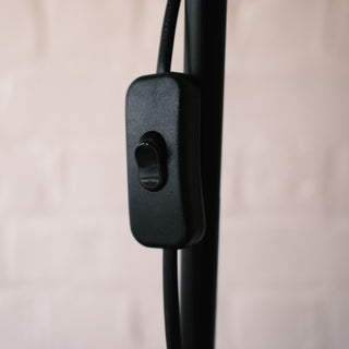 Close up of the black inline switch on the Luma Pleated Floor Lamp, attached to the power cord and pole with soft background blur.