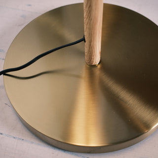 Close up of the Luma Pleated Floor Lamp’s brushed brass base with a natural wood pole and black cord detail.