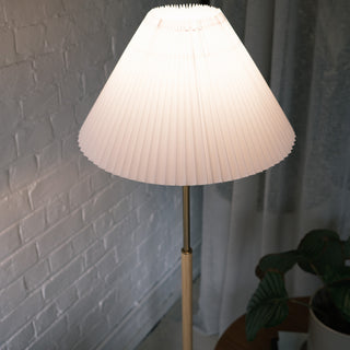 Close up of the Luma Pleated Floor Lamp’s wide pleated fabric shade glowing warmly in a cosy interior setting.