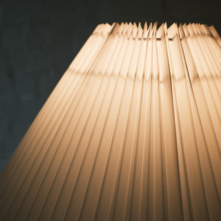 A close up view of the Luma Floor Lamp’s white pleated fabric shade, showing the fine folded texture illuminated by warm light, creating a soft and elegant glow.