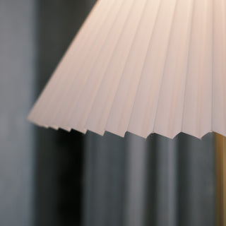 Close up of the Luma Floor Lamp’s pleated fabric shade, showing the crisp folded edges and soft white texture against a blurred interior background.