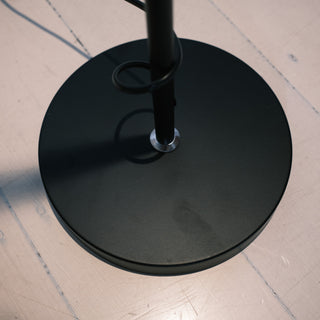 Close up of the Lumen Duo Floor Lamp’s sturdy matte black base with central pole and cord wrap, shown on a light timber floor.