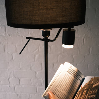 Close up of the Lumen Duo Floor Lamp showing the focused reading light illuminating an open book, with the textured black fabric shade and metal frame creating a warm, cosy atmosphere.