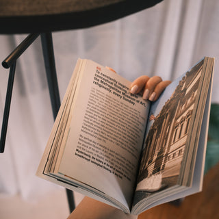 A person holding an open book under the focused reading light of the Lumen Duo Floor Lamp, with the lamp’s arm and shade subtly visible in the background.