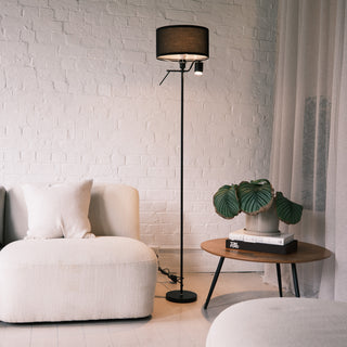 The Lumen Duo Floor Lamp placed beside a soft cream lounge chair and a wooden side table with greenery, creating a warm and modern living room atmosphere.