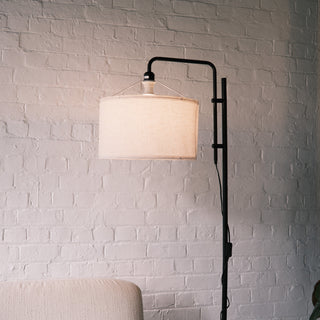 Close up of a modern standing lamp featuring a soft fabric drum shade and a matte black metal frame, styled against a white brick wall. A clean NZ home setting ideal for floor lamps, standing lamps, modern floor lamps and dimmable lamp collections. | C&F Creation NZ