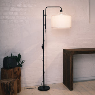 Full view of the Madox Loft floor lamp standing beside wooden stools and a minimalist console table, featuring a black metal frame and warm fabric shade. Ideal for floor lamps NZ, standing lamps, modern floor lamps and dimmable lamps. | C&F Creation NZ