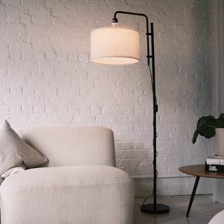 Modern black standing lamp with an adjustable arm and a soft fabric drum shade, styled beside a cream lounge chair in a contemporary NZ living space. Ideal for homes looking for floor lamps, standing lamps, modern floor lamps or dimmable lamp options. | C&F Creation NZ